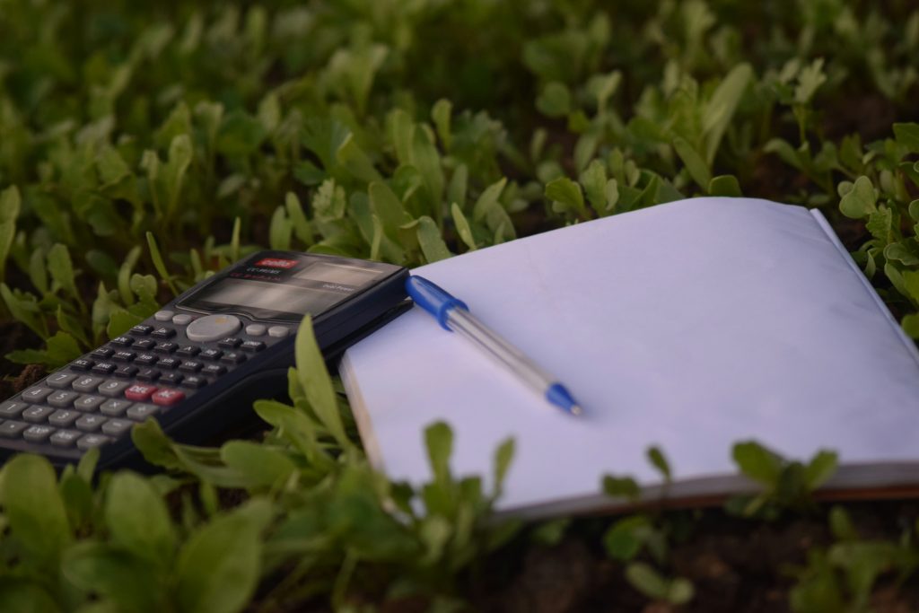 A calculator, a pen and a notepad placed amongst some green grass